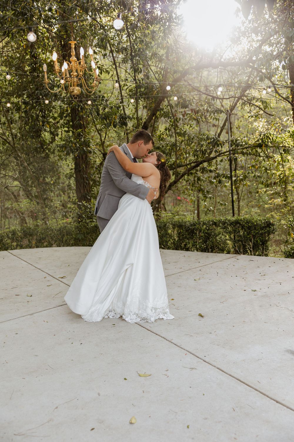 A romantic couple shares a tender moment on a sunlit patio surrounded by lush greenery and trees.