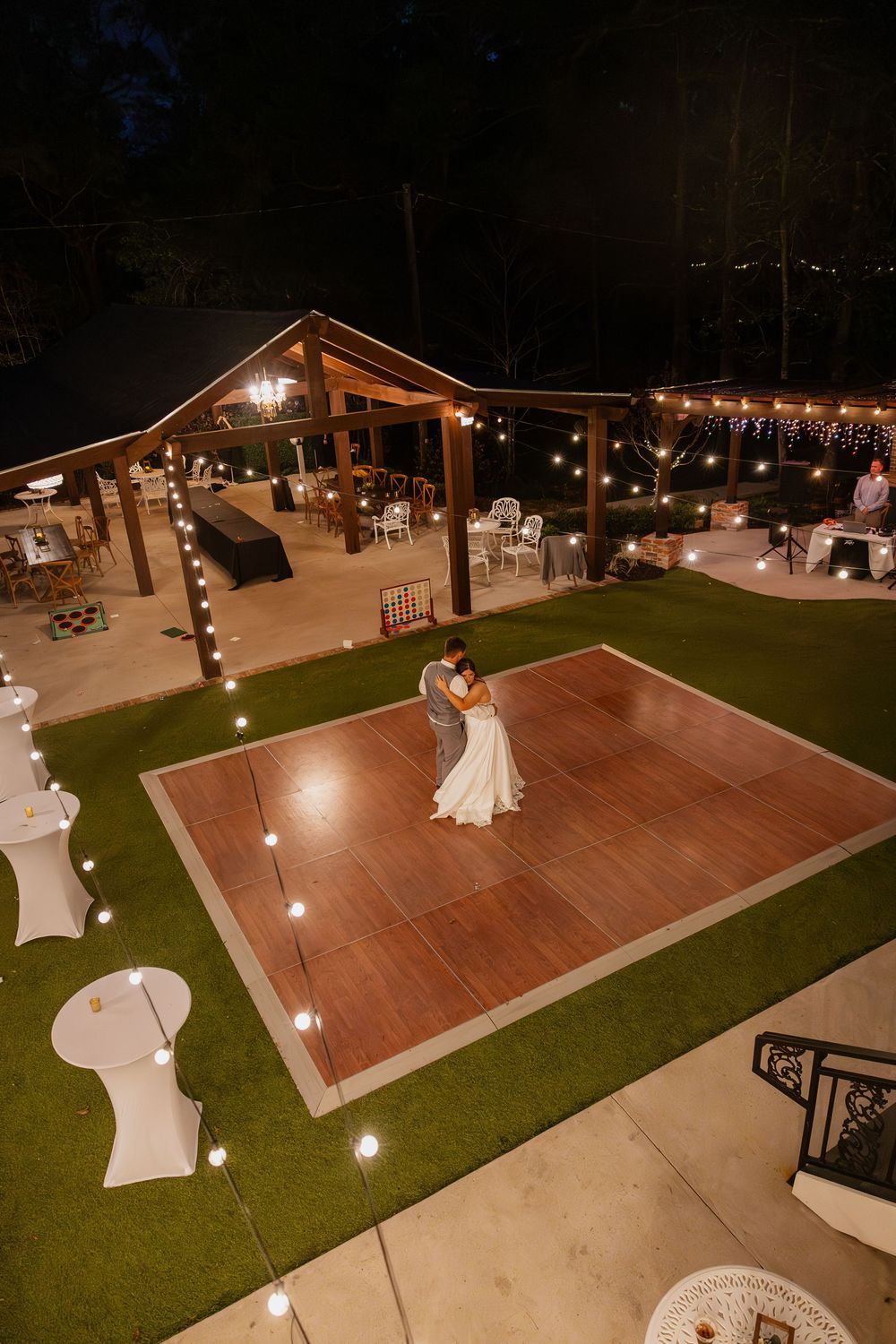 Aerial view of an outdoor wedding reception space with a wooden dance floor and string lights at night.