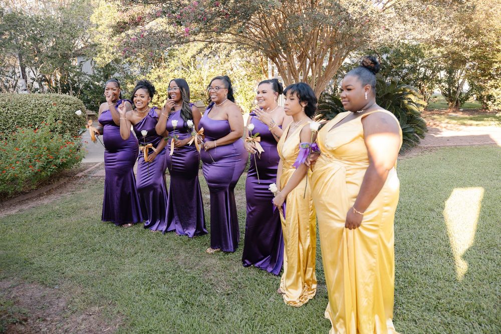 Wedding party in purple and gold dresses posing outdoors on a sunny day.