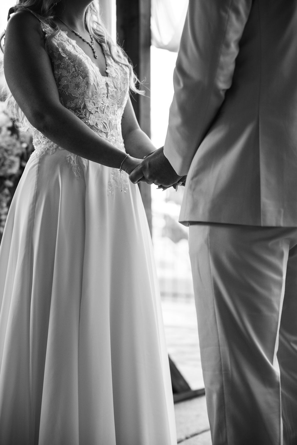 Black and white wedding ceremony photo showing couple holding hands at the altar in elegant white dress and suit.
