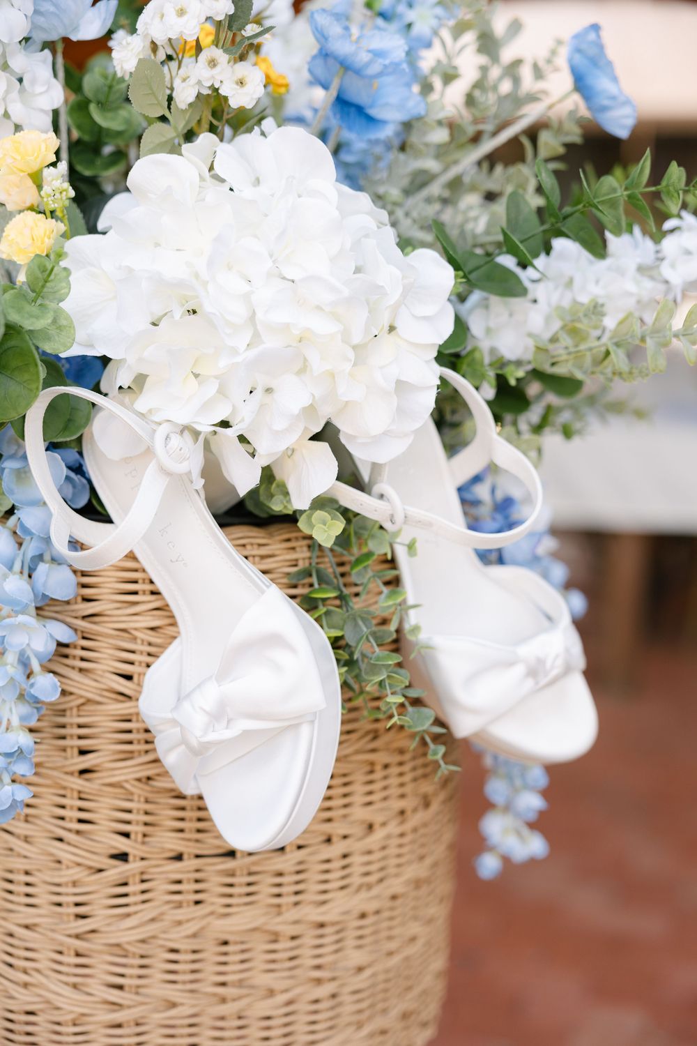 A woven wicker basket filled with delicate white and blue flowers arranged in a romantic floral display.