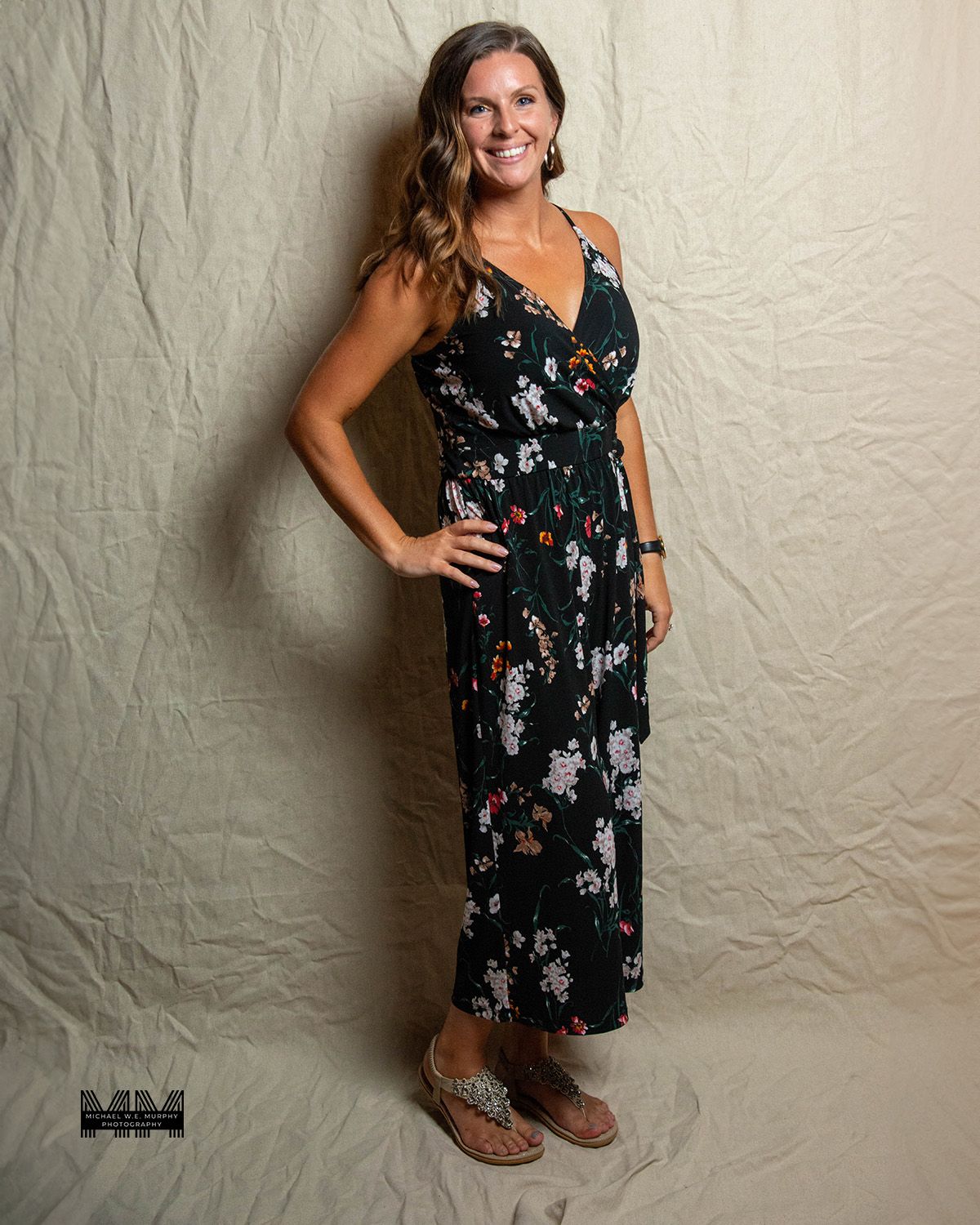 Portrait of person in floral maxi dress standing against neutral backdrop.
