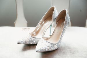 Elegant white lace wedding heels with pointed toes displayed on light surface.