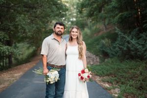 Couple stands together on wooded path holding floral bouquets representing blue for baby boy and pinks for baby girl in gender reveal shoot