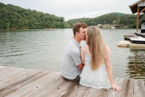 Intimate moment shared between couple sitting on lakeside dock during summer.
