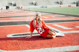 Graduate poses on vibrant red and black end zones of a football field.