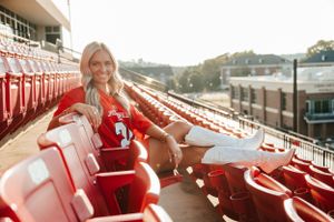 Graduate wearing white shorts relaxes in red stadium seats during golden hour.