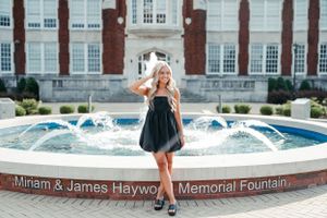 Graduate poses by the Miriam & James Hayword Memorial Fountain on a sunny day.