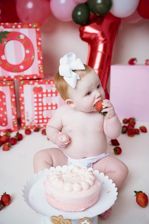 Sweet white and red cake smash setup with strawberries, balloons, and pink decor for first birthday celebration.