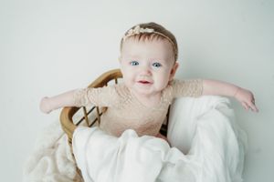 Baby in beige outfit sitting in vintage chair with white linens.