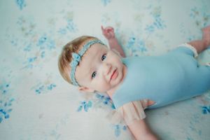 Baby wearing blue outfit on floral background with matching headband.