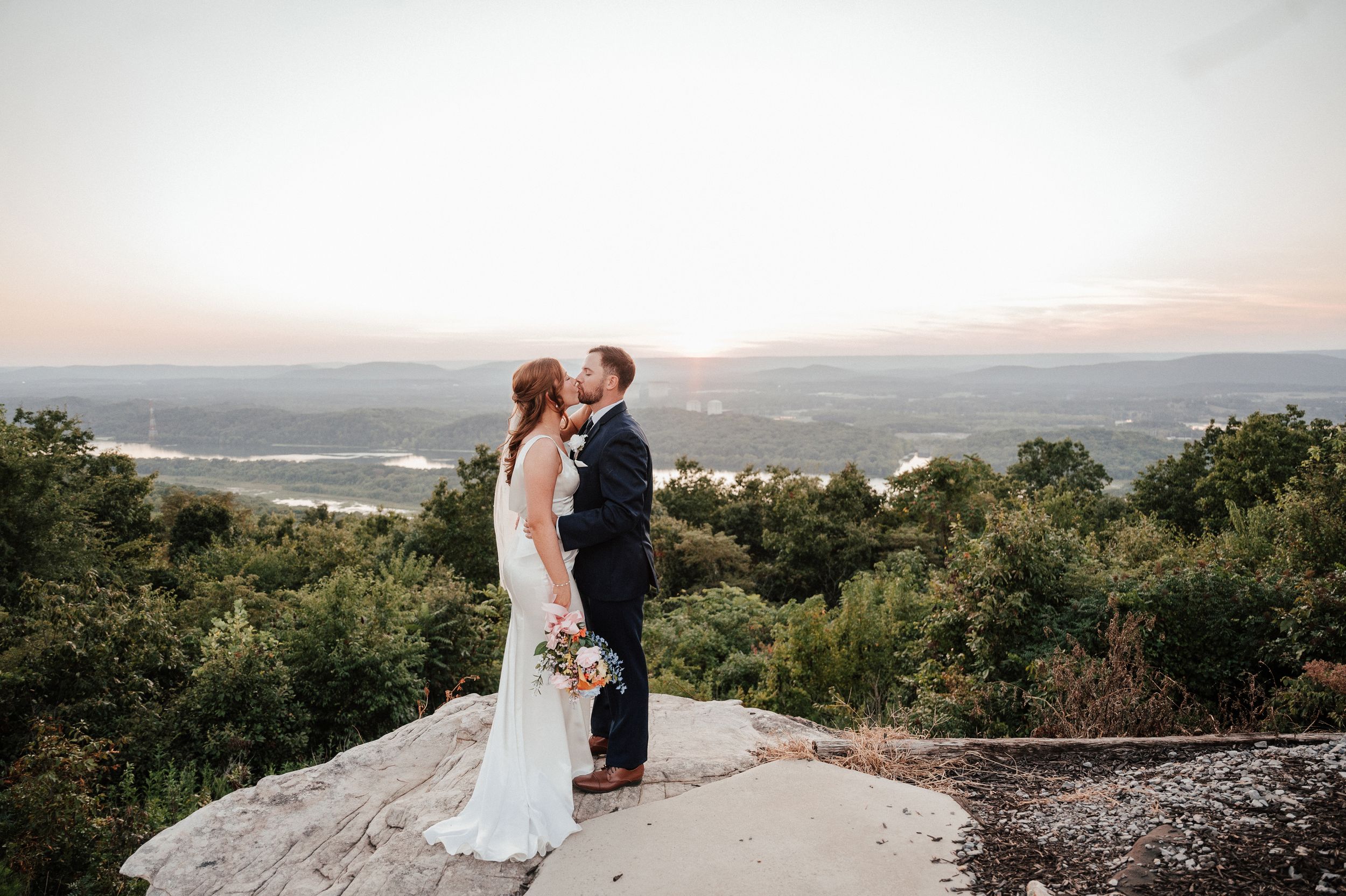 Couple sharing a romantic moment at scenic mountain overlook during sunset.