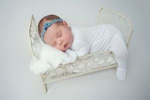 Sleeping baby in white sleeper on vintage metal bed with blue headband.