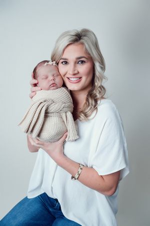Tender studio portrait with sleeping newborn baby wrapped in knit blanket.