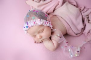 Sleeping newborn baby wearing sparkly headband on pink fabric background.