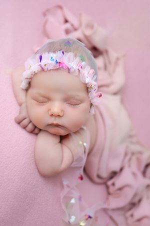 Close-up of peaceful sleeping baby wearing pink and blue crystal headband on pink background.