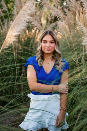 Portrait in blue top and white skirt against tall ornamental grasses at golden hour.