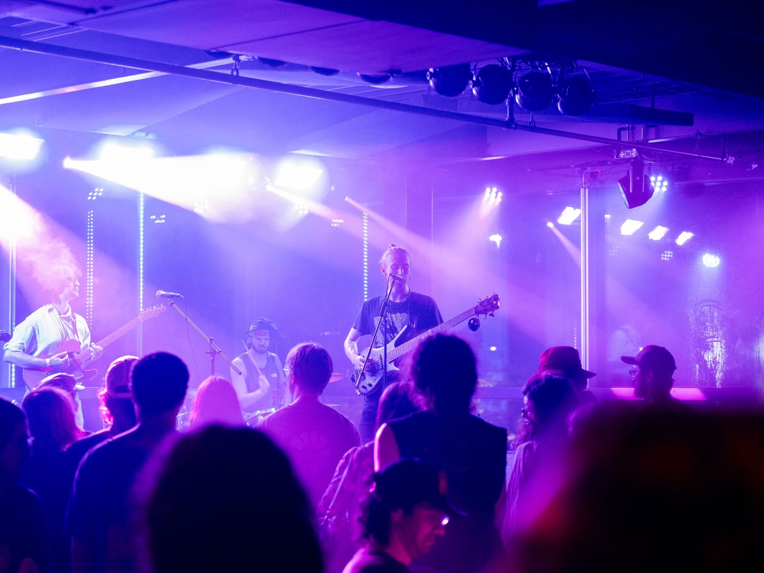 A crowd of people dance in a nightclub with purple lighting and atmospheric smoke effects creating a vibrant atmosphere.