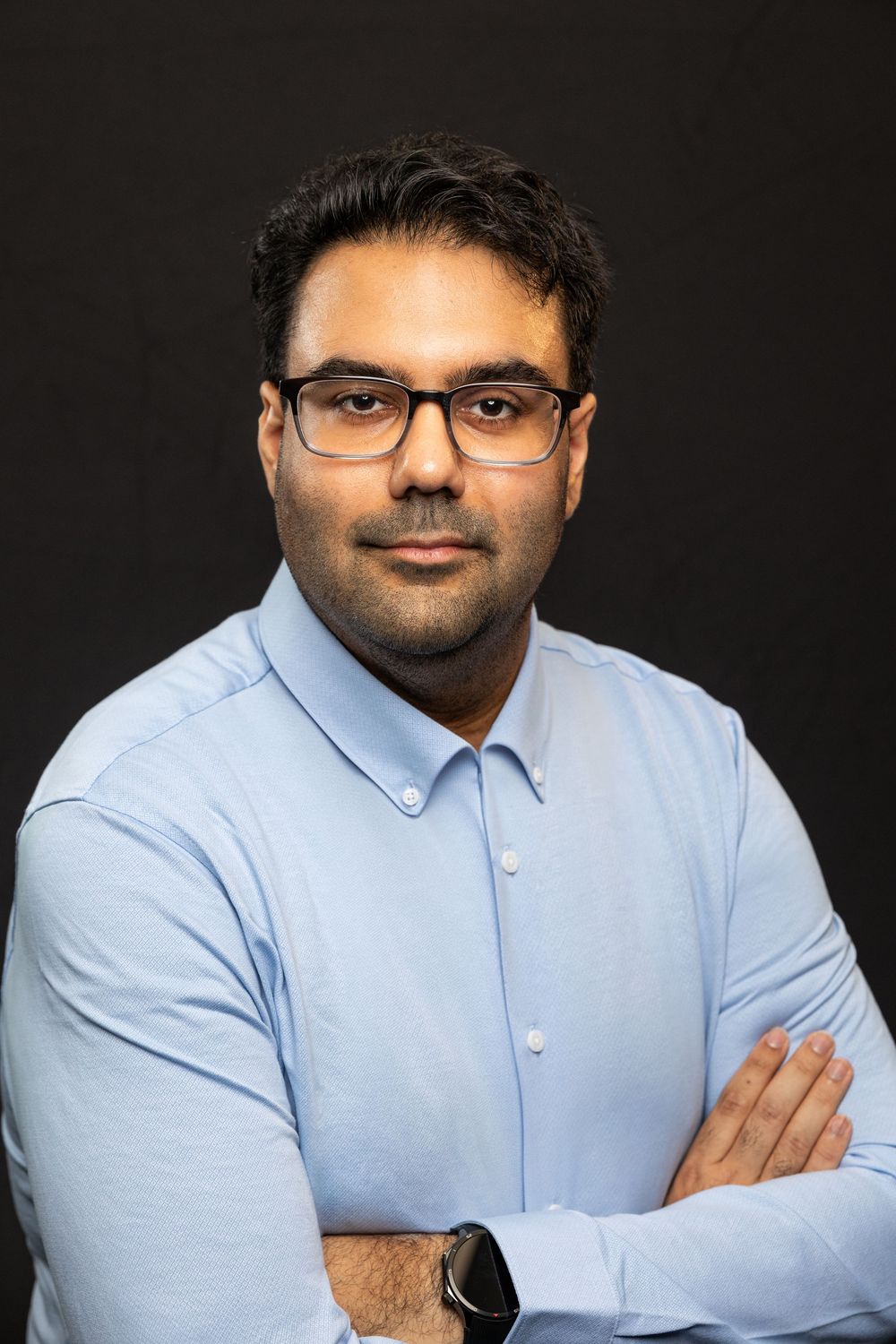 Professional headshot series showing different poses in a light blue button-down shirt against dark background.