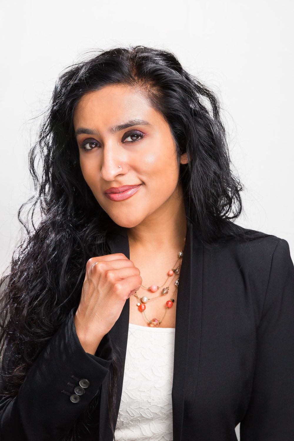 Business professional poses in black blazer and white top against white backdrop.