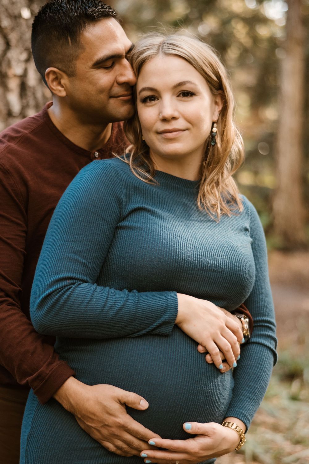 Intimate maternity photos showing a couple embracing in a forest setting.