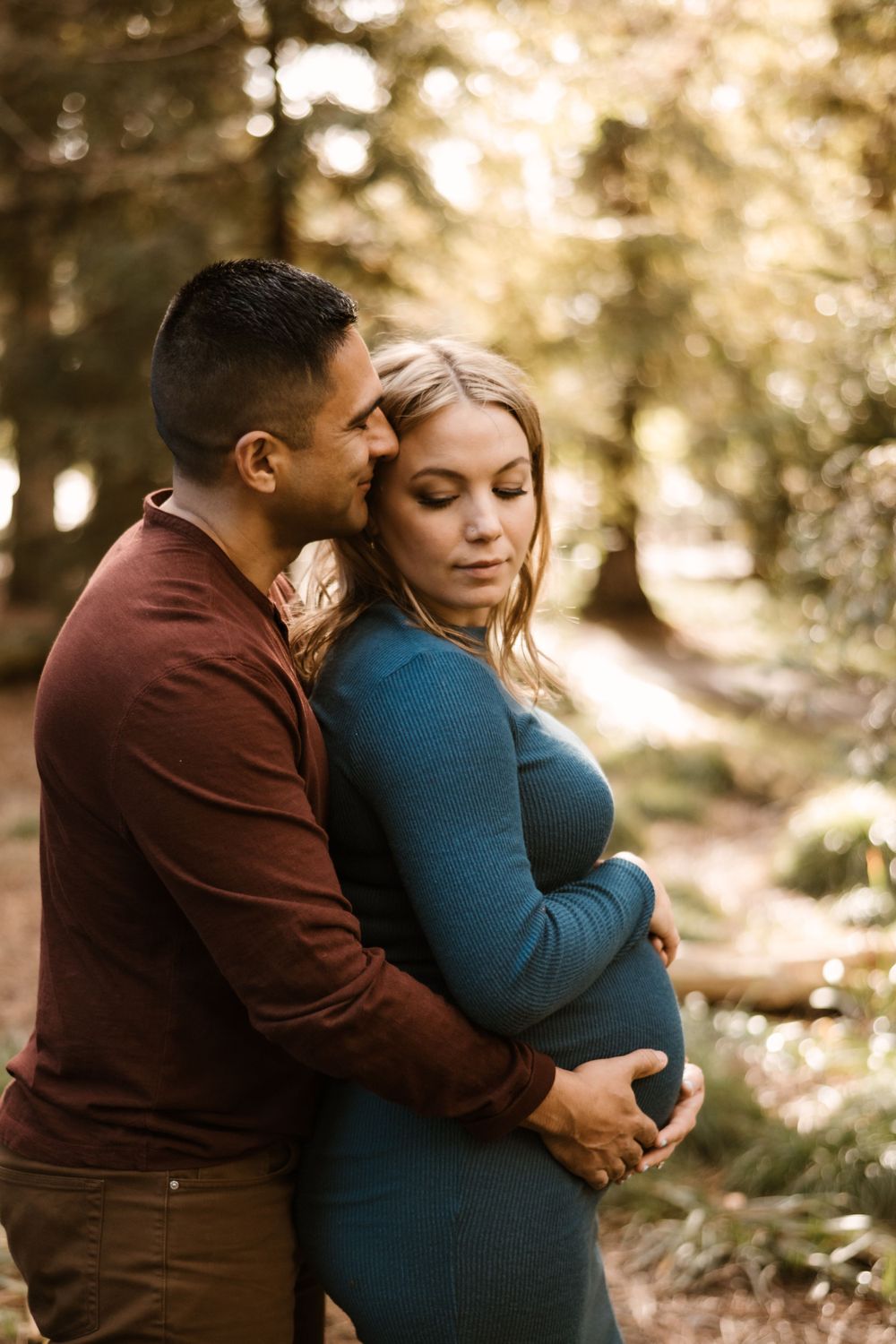 Tender maternity portraits showing gentle embraces among pine trees.