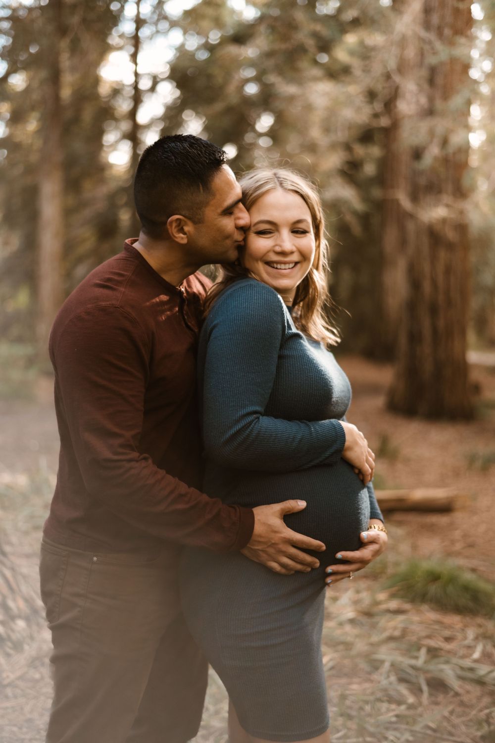 Loving maternity photography session in a golden-lit forest setting.