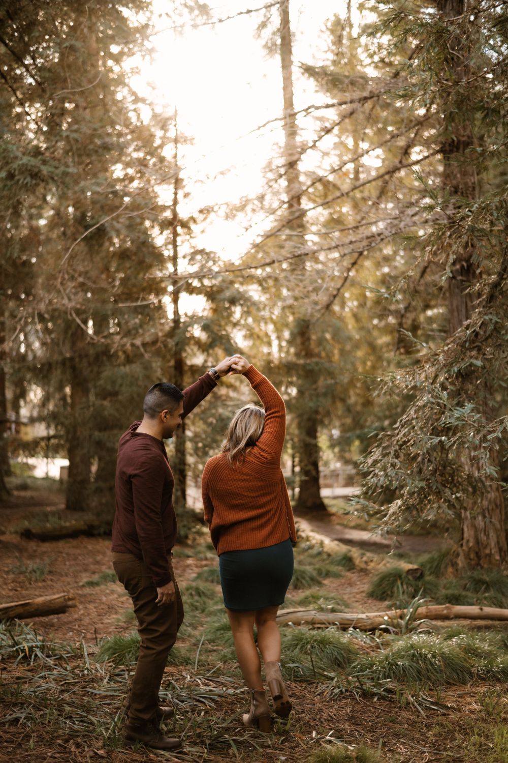 Playful maternity photoshoot with couple dancing in a forest.