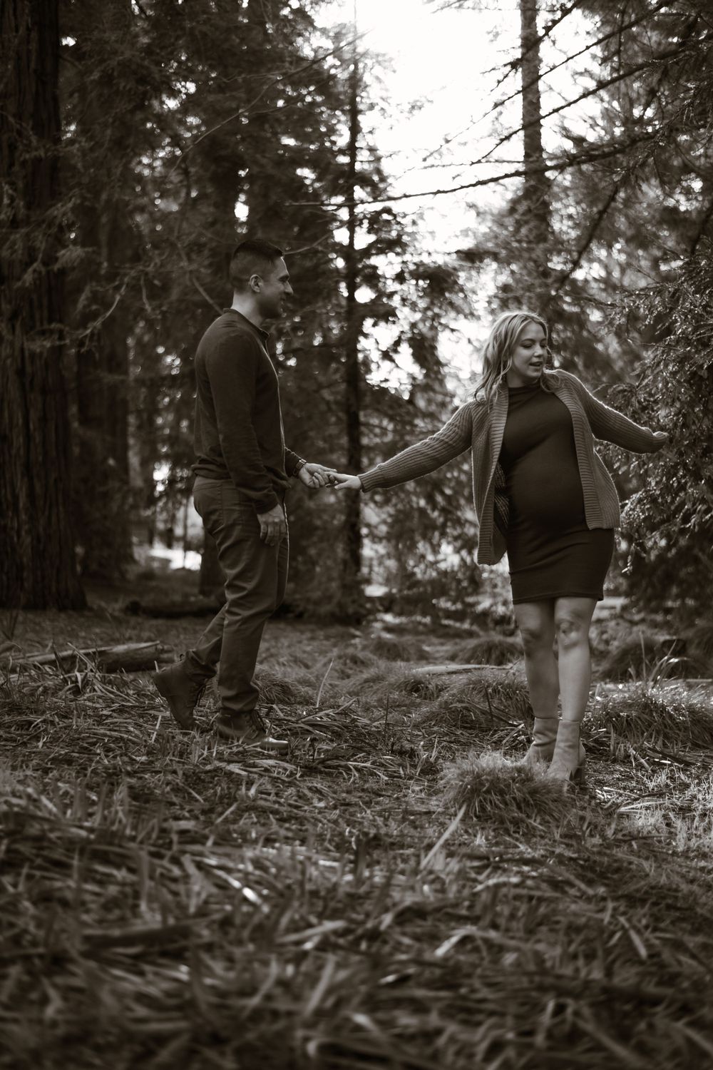 Black and white maternity photos showing couple walking through forest.