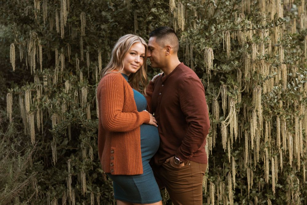 Romantic couple in warm sweaters share intimate moments outdoors among moss-draped trees.