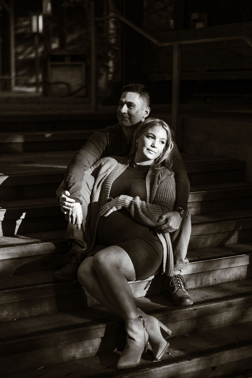 Intimate black and white maternity photoshoot with couple on wooden floor.