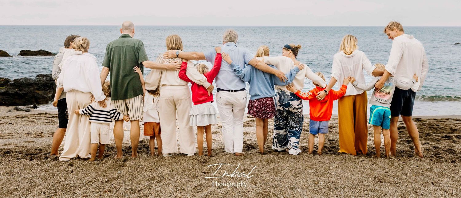 Large family standing together on the beach with their backs to the camera, arms wrapped around each other.