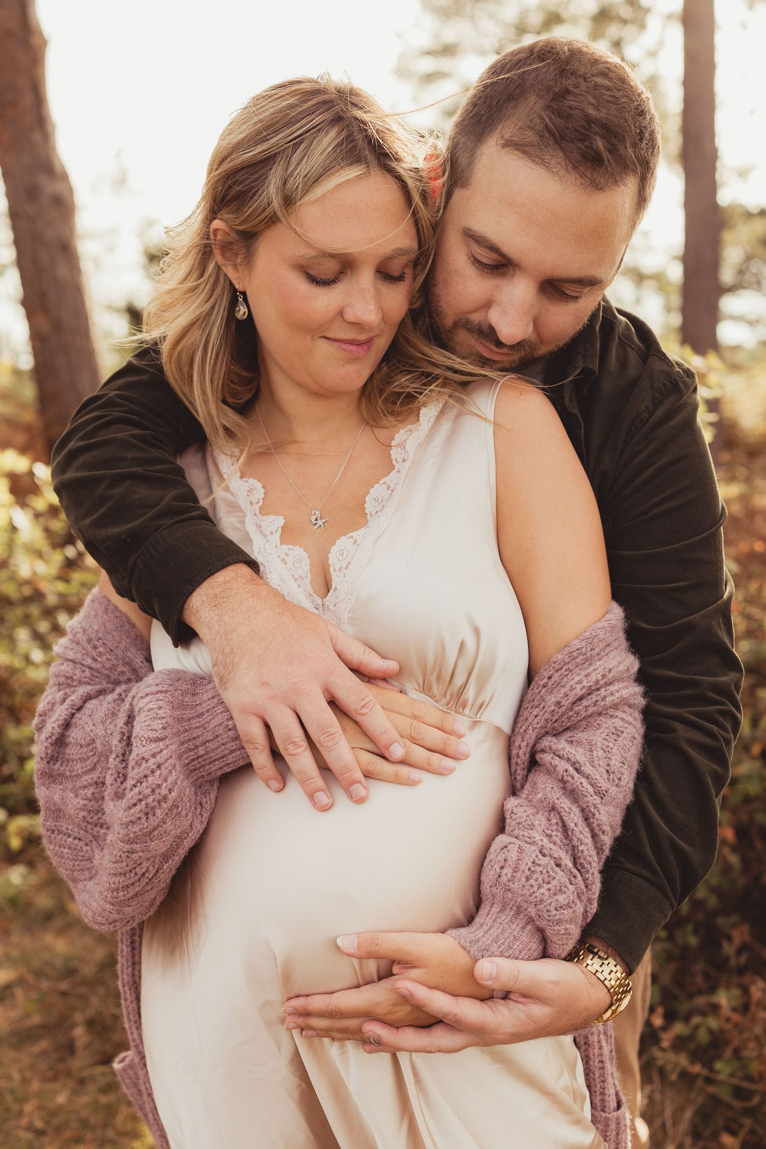 Couple shares intimate moment during sunset maternity photoshoot in golden field.
