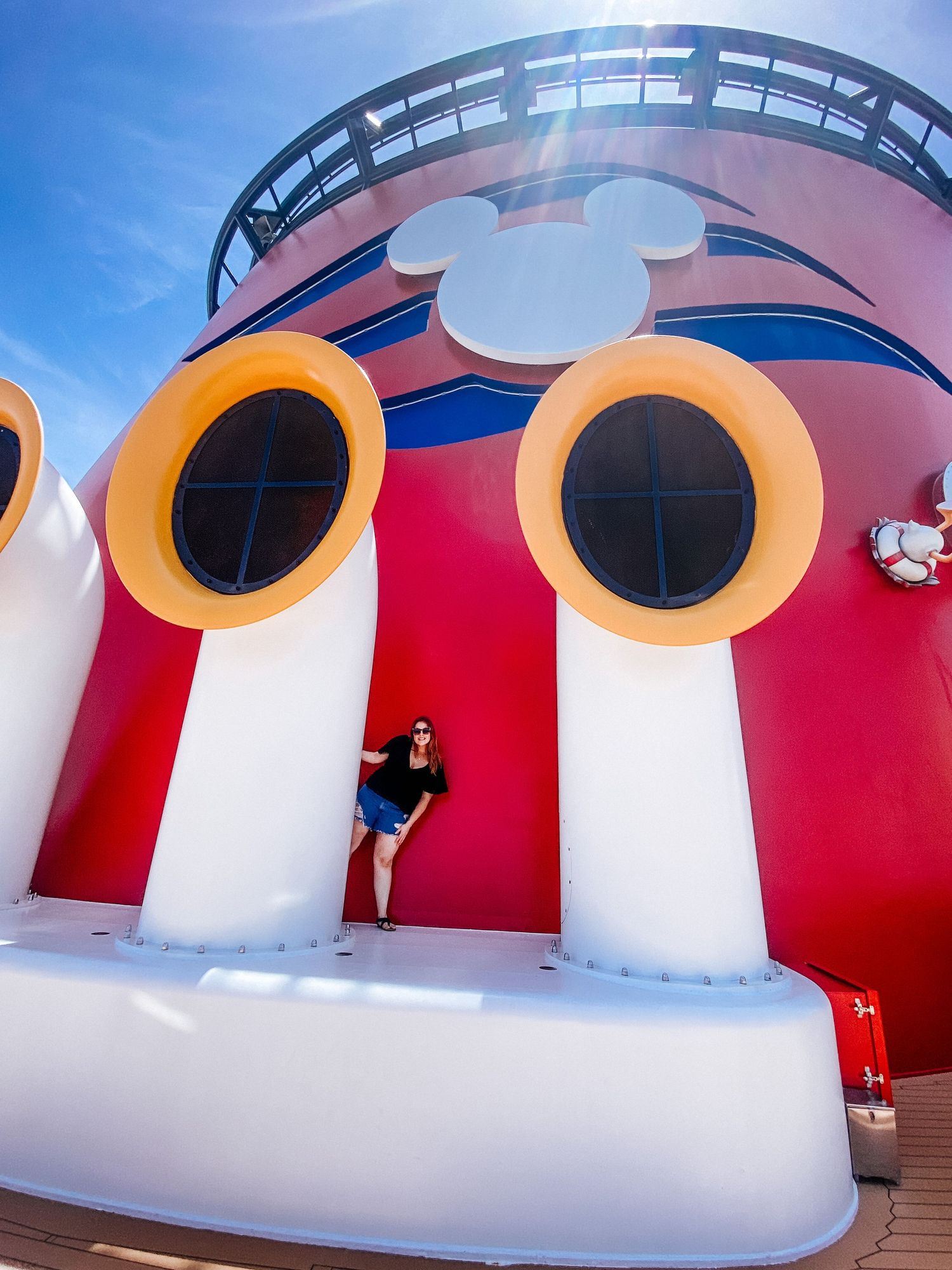 Woman posing on Disney Cruise ship deck beside iconic Mickey Mouse funnel in red and white.