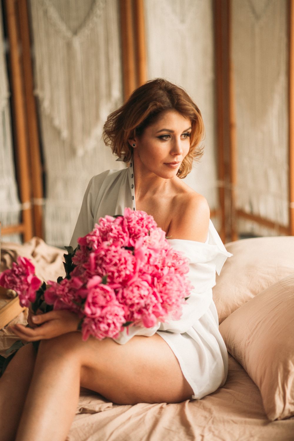 A figure in white reclines on a beige couch with vibrant pink peonies.