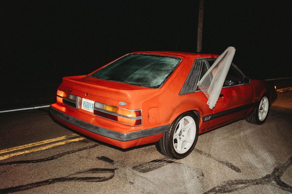 Vintage red Ford Mustang GT hatchback parked on dark road at night after wedding celebration.