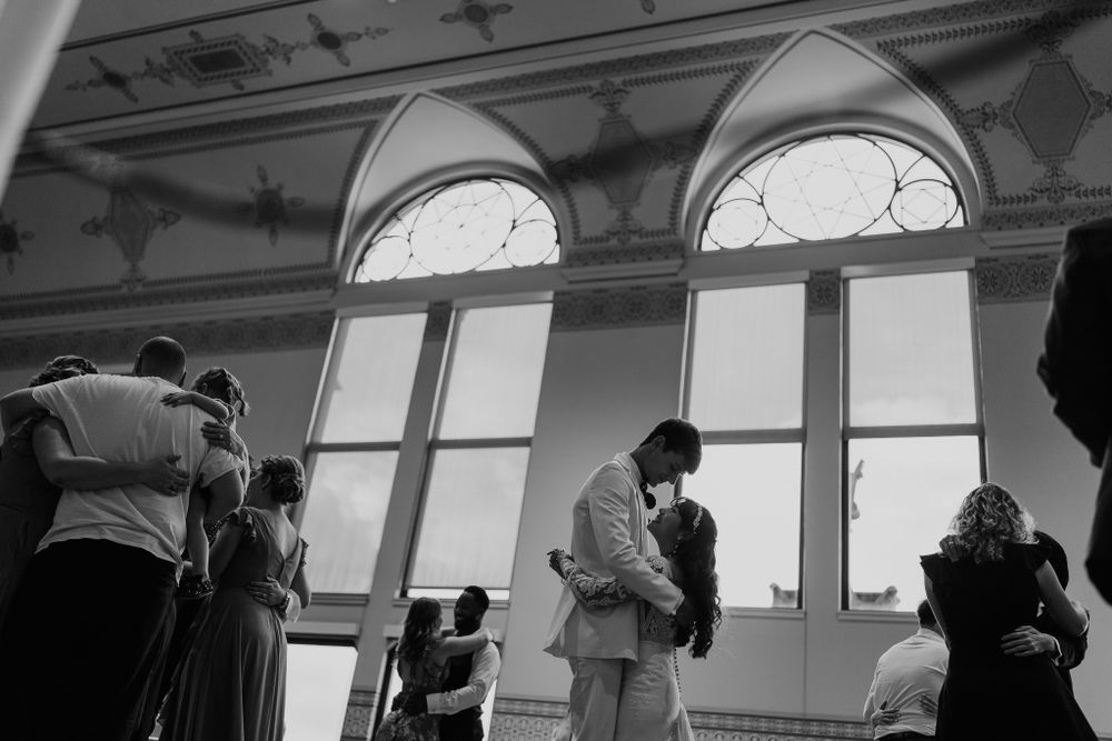 Black and white photo of couples dancing in an elegant ballroom with arched windows during a wedding reception.