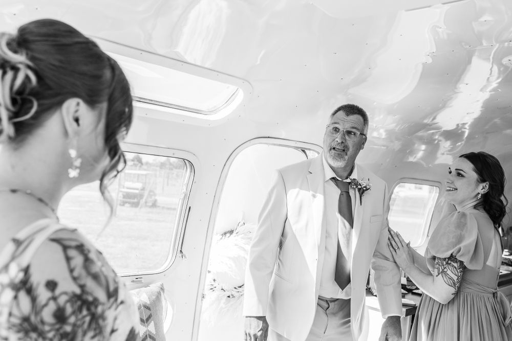 Black and white photo of a groom in white suit chatting with guests inside a vehicle.