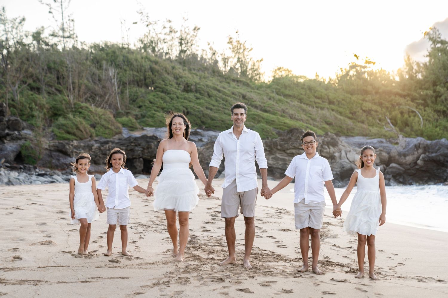 Large group poses together on a scenic Hawaiian beach with waves and coastline in background.