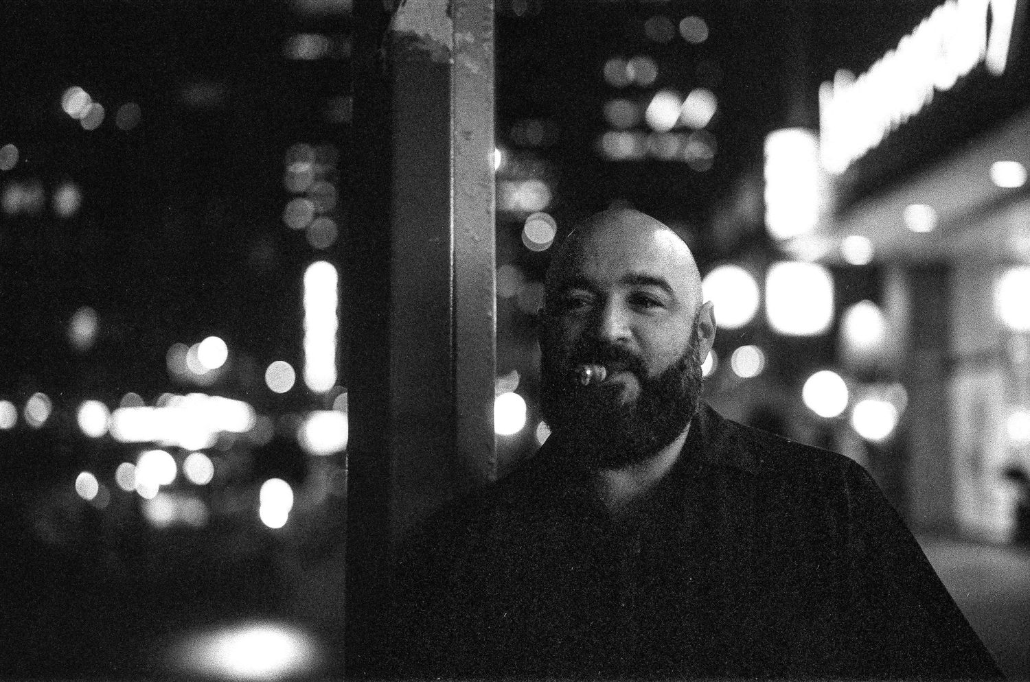 Black and white nighttime portrait of person smiling with city lights in background.