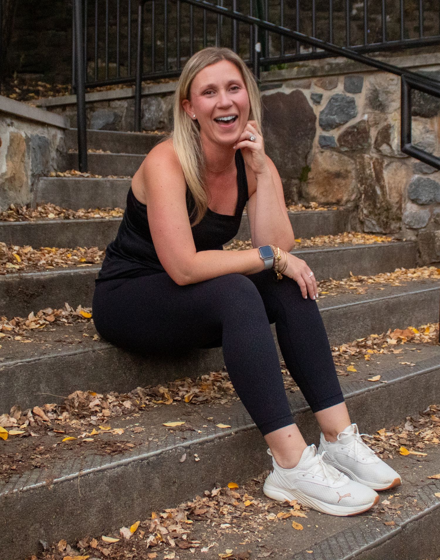 Candid portrait sitting on stone steps wearing black athletic wear and white sneakers.