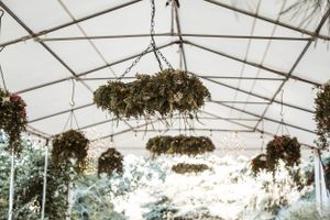 Hanging floral arrangements and greenery decorate the ceiling of a white outdoor wedding tent.