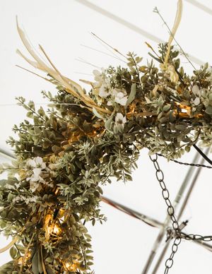 Rustic floral chandelier with antlers and greenery illuminated by warm lights hanging from a chain.