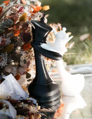 Black and white chess pieces arranged with dried flowers and autumn decorations.