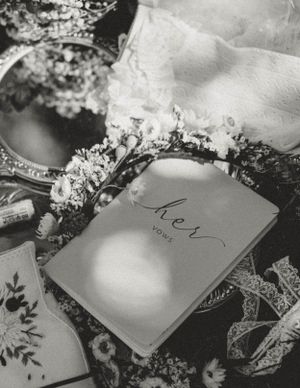 A black and white still life of wedding vows book with lace and floral decorations.