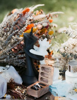 Wedding decor featuring chess pieces, a wooden ring box, and dried flowers in warm autumn colors.