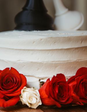 A white frosted cake decorated with vibrant red roses and a single white rose along the base.