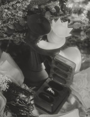 A black and white photograph of an engagement ring box nestled among delicate flowers and lace.