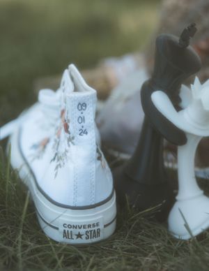 A white Converse All Star sneaker rests on grass with a blurred background.