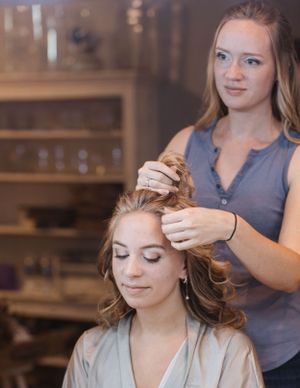 A hairstylist styles a client's hair in a salon setting with warm lighting and wooden decor.